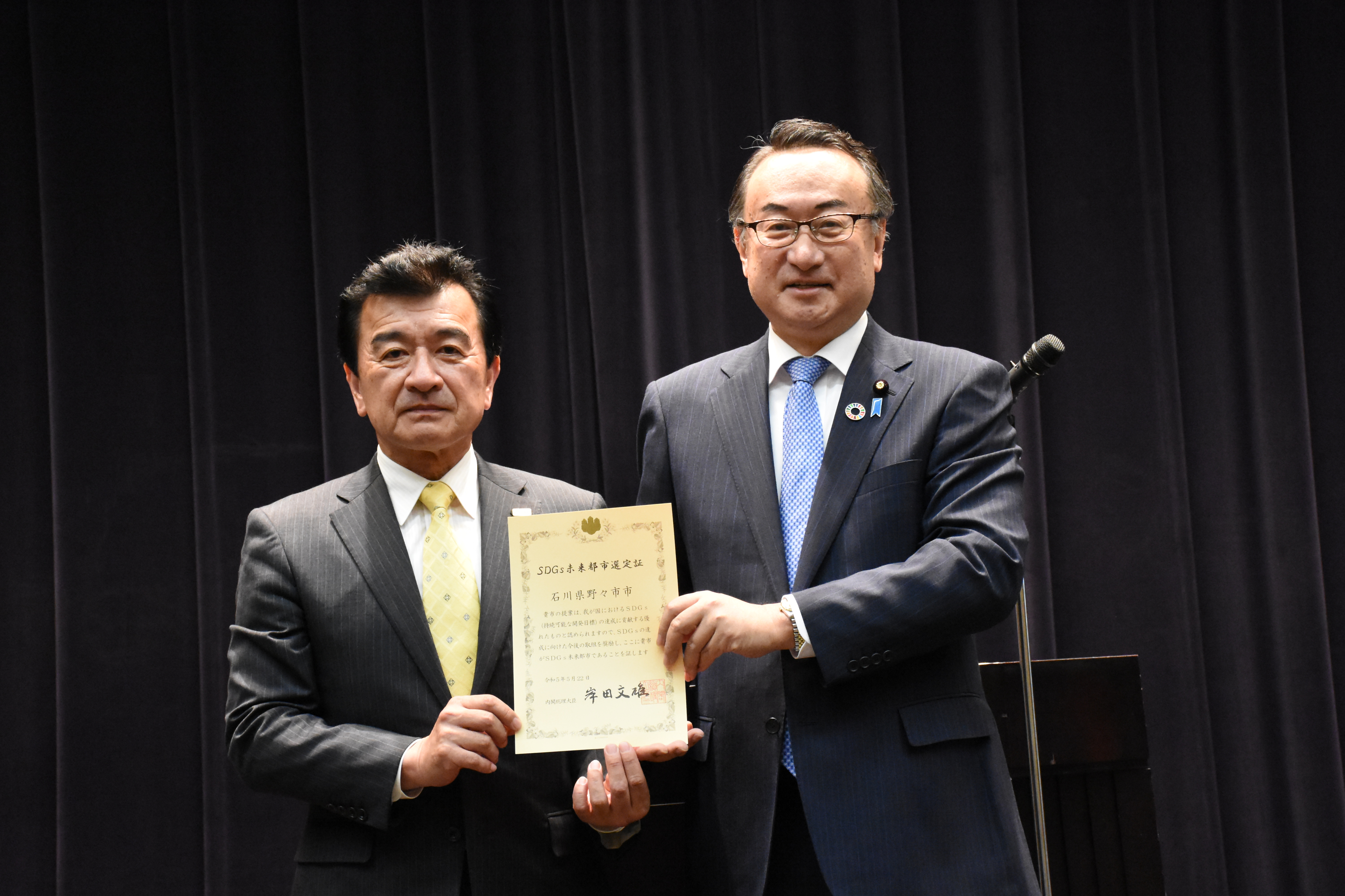 選定証授与式の写真（岡田大臣と粟野々市市長）