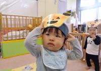 自分の足型で作ったかぼちゃのお面をかぶっている０歳児