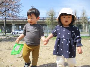 園庭で友達と手をつないで歩く１歳児