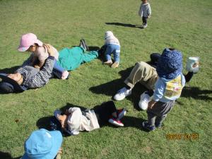 芝生に寝転がって遊ぶ1歳児と保育士