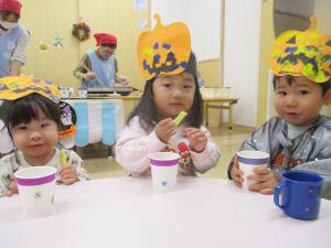 ハロウィンでかぼちゃのお面を被って園で採れたさつまいもを食べる１歳児