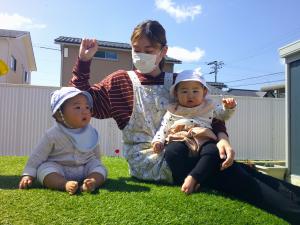 園庭の築山で保育士を一緒に日向ぼっこをする０歳児